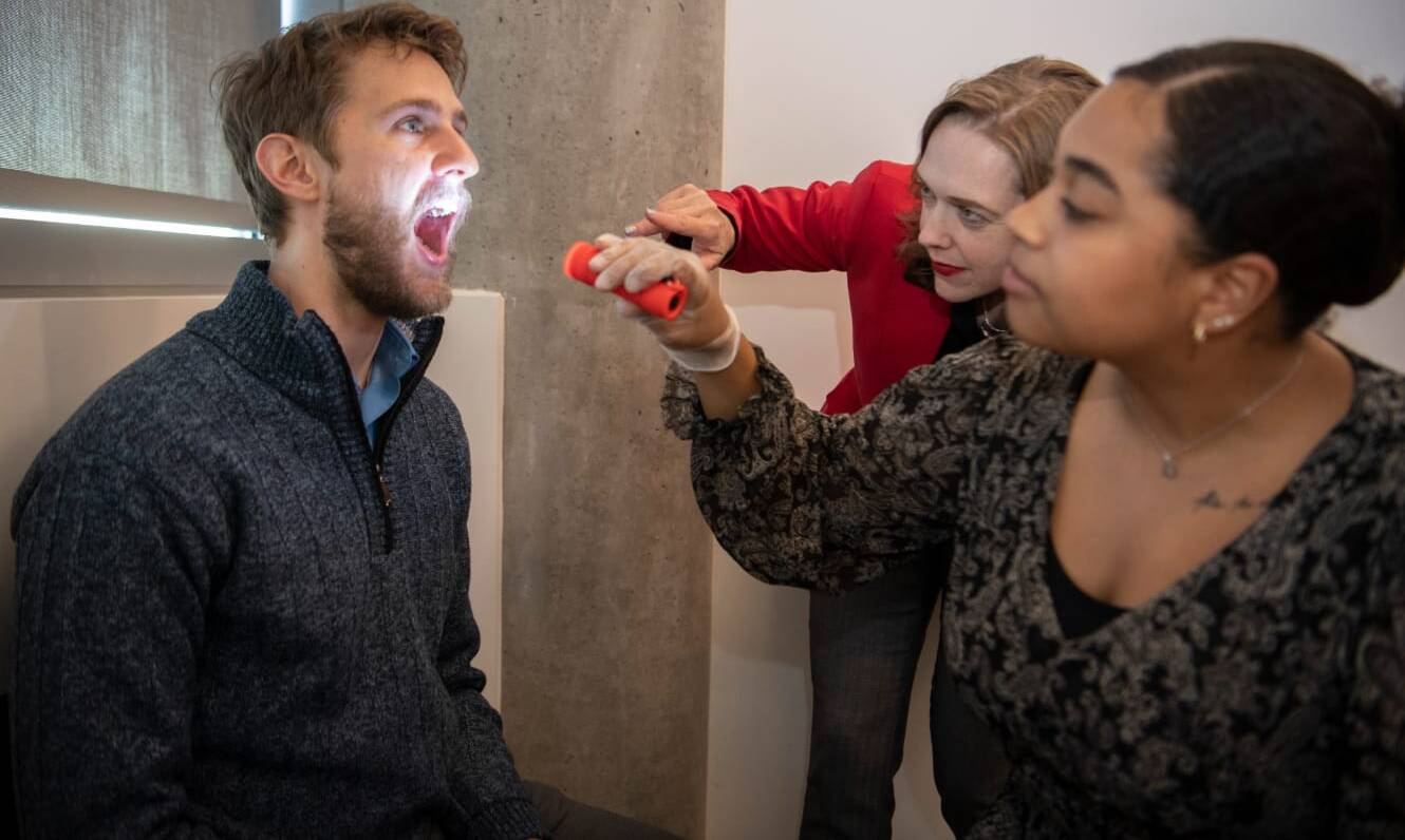 Two speech pathologists observe the inside of a man's mouth.