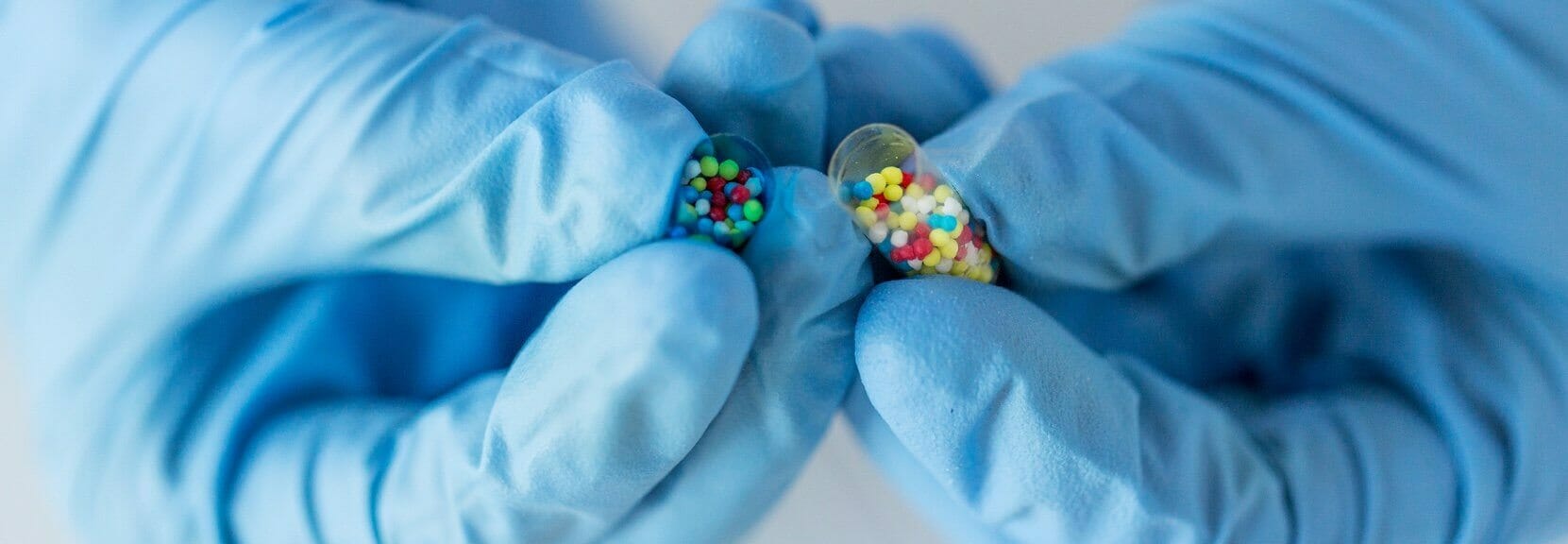 A pair of gloved hands each holding a pill.