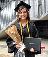 Pre-Occupational Therapy student celebrating graduation wearing a cap and gown, posing with her diploma and a bouquet of flowers.