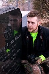 Pre-Occupational Therapy student Anthony squatting down observing a Navy Armed Guard headstone.
