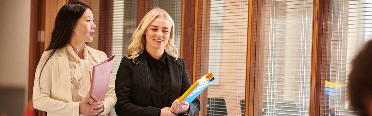 Two paralegals walking in an office holding folders.