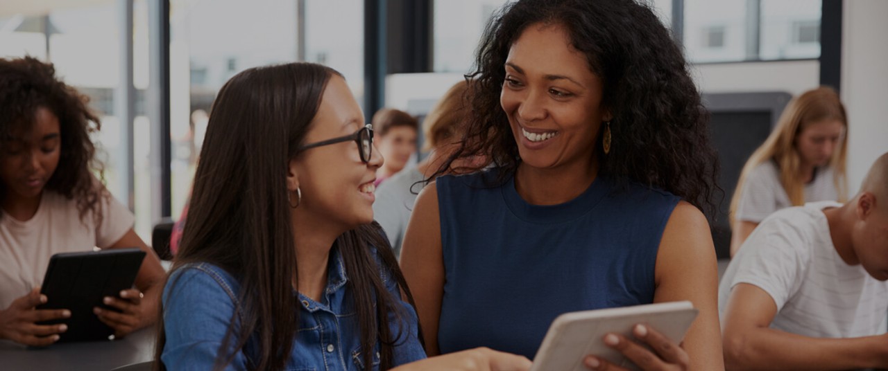 A principal looks at a student and smiles while holding a tablet.